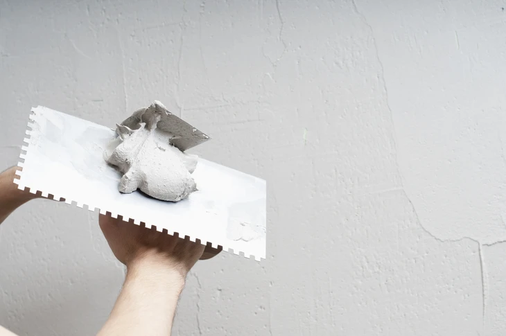 Chantier de ma&ccedil;onnerie en ext&eacute;rieur, ouvrier en gants tenant un marteau pour ajuster des briques rouges